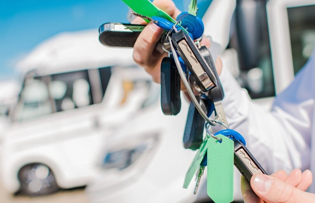 mehrere Fahrzeugschlüssel in der Hand eines Caravanhändlers, im Hintergrund Wohnmobile